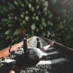 A man poses daringly over train tracks with a forest view.